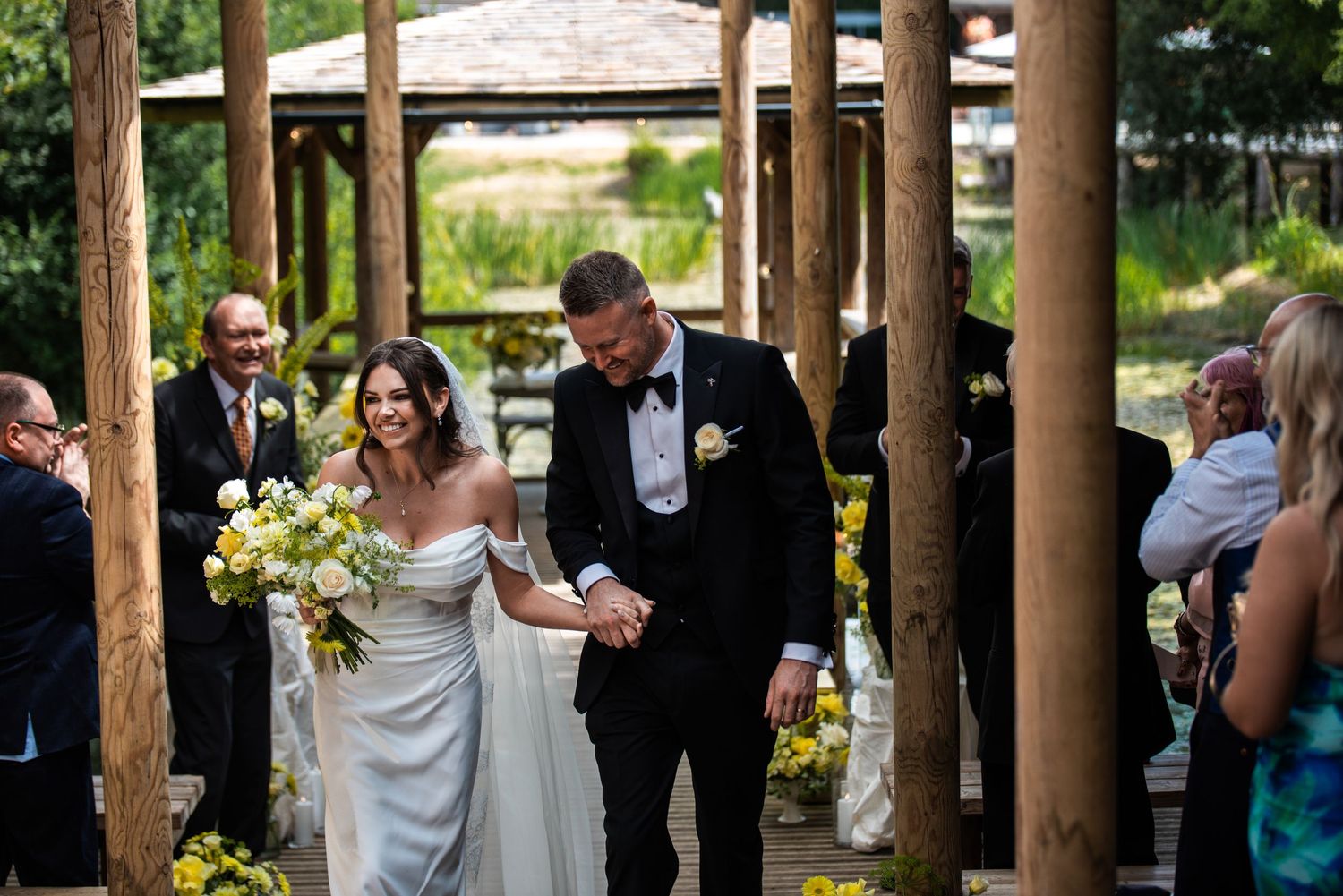Bride and groom smiling and holding hands as they walk down the aisle at an outdoor wedding ceremony at Oaklands.