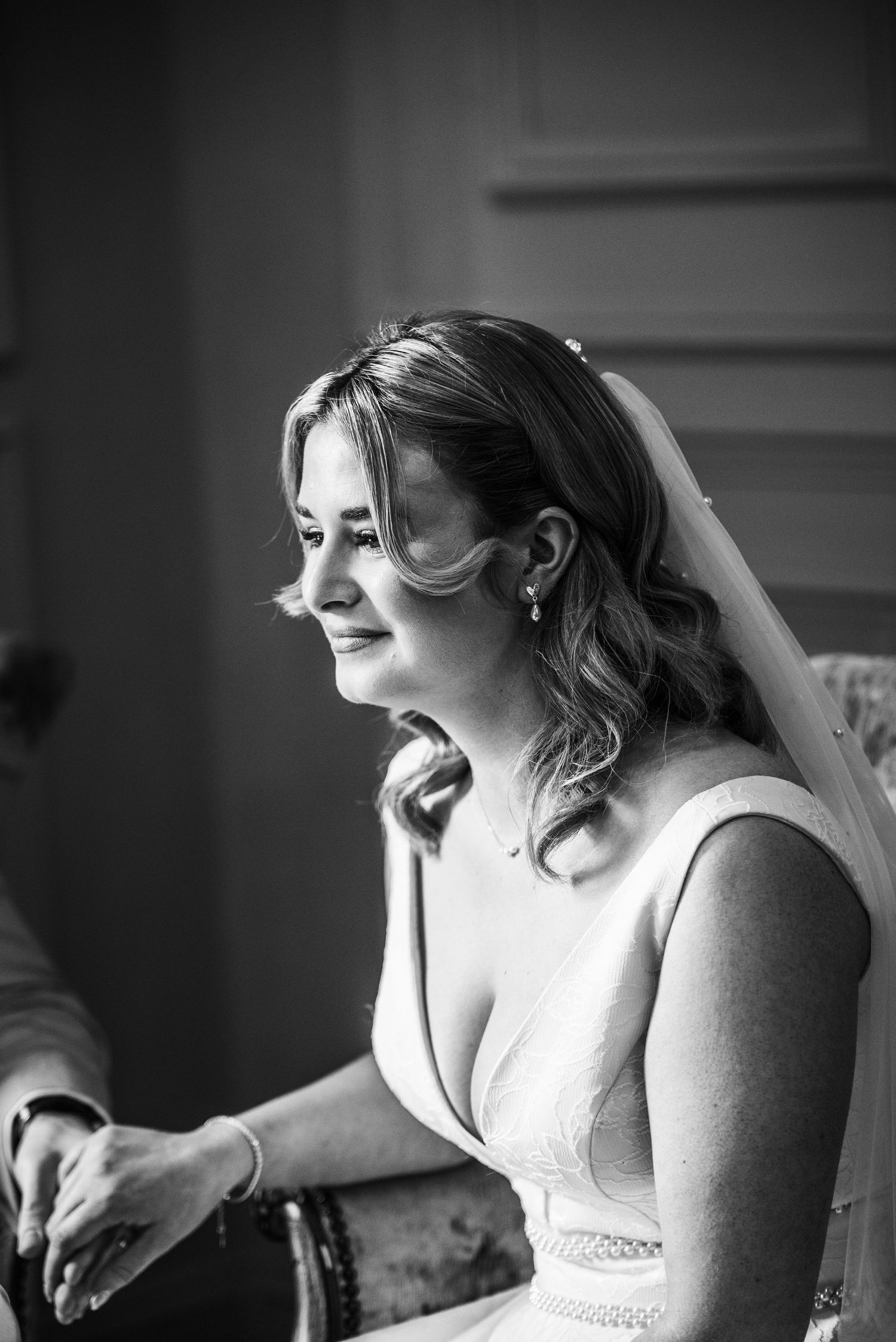 Black and white photo of a bride in a wedding dress and veil, smiling emotionally during wedding preparations.