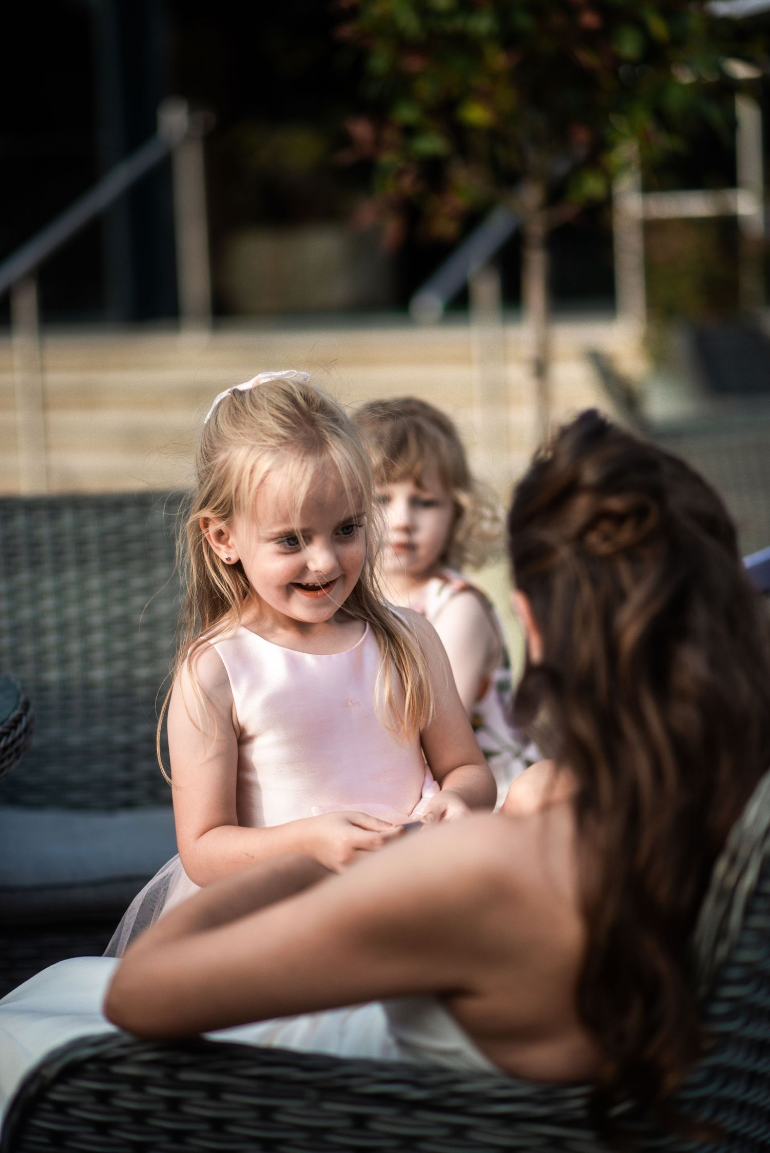 Young blonde girl in white dress smiling at a woman during an outdoor event with children.