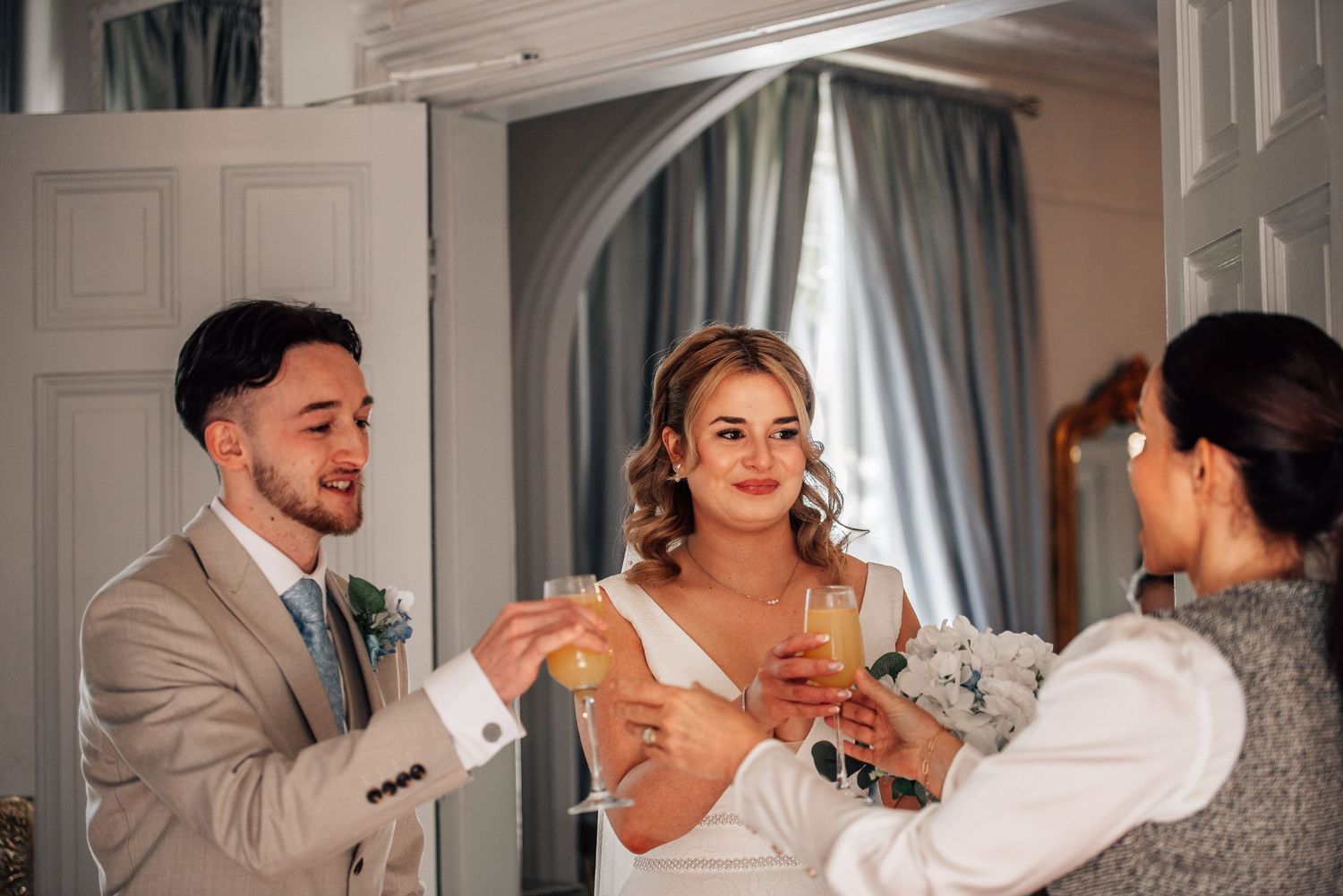 Bride and groom toasting champagne with a guest in a elegant room during their wedding celebration.