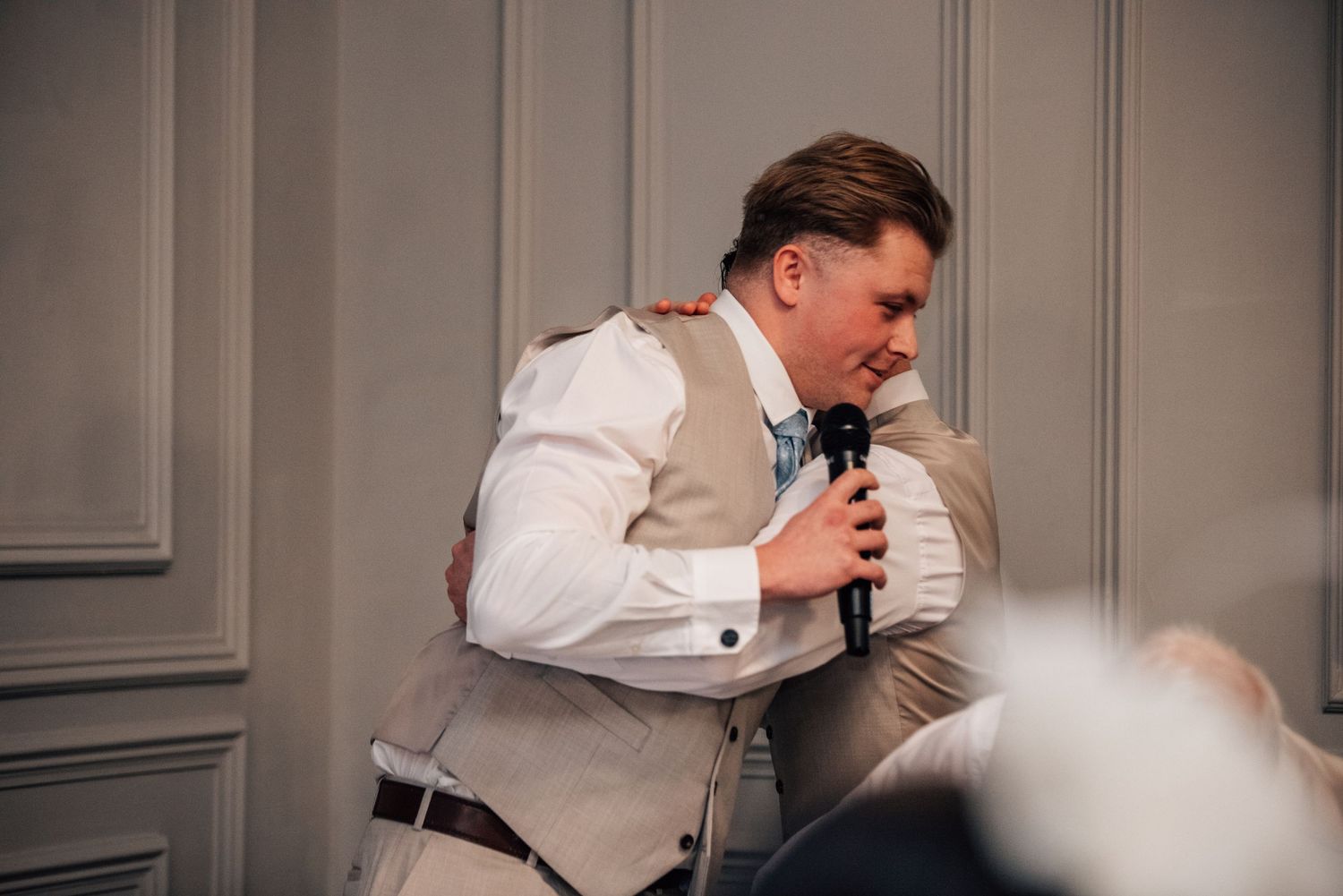 Man in white shirt and vest speaking into microphone at a wedding reception event.