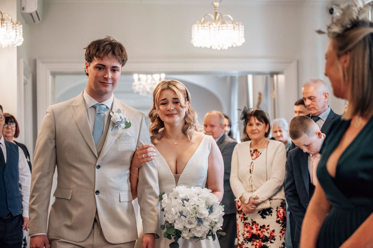 Bride and groom walking down the aisle together at an elegant wedding ceremony with chandelier lighting.