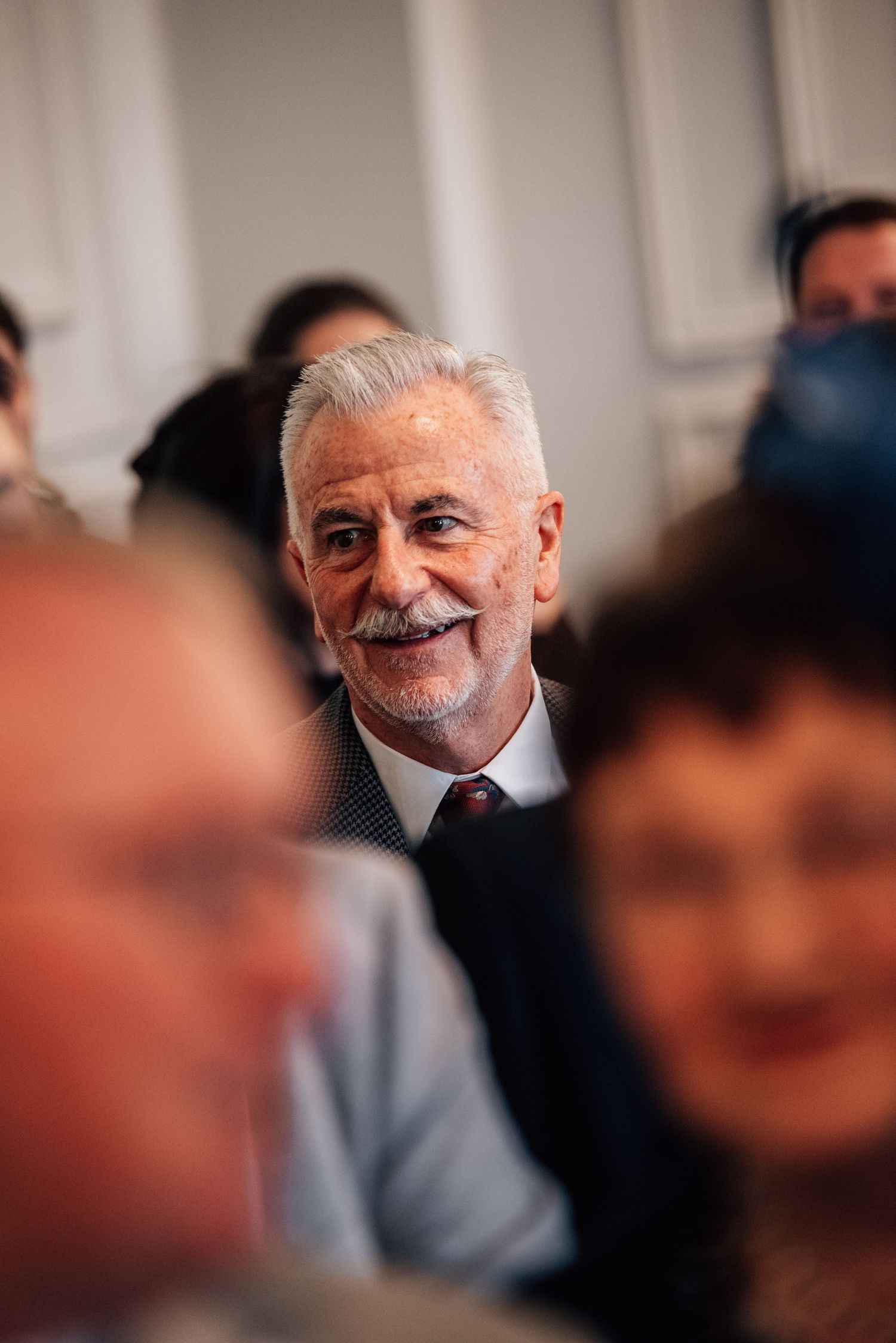 Smiling older gentleman with gray hair and mustache wearing a suit at a wedding ceremony.