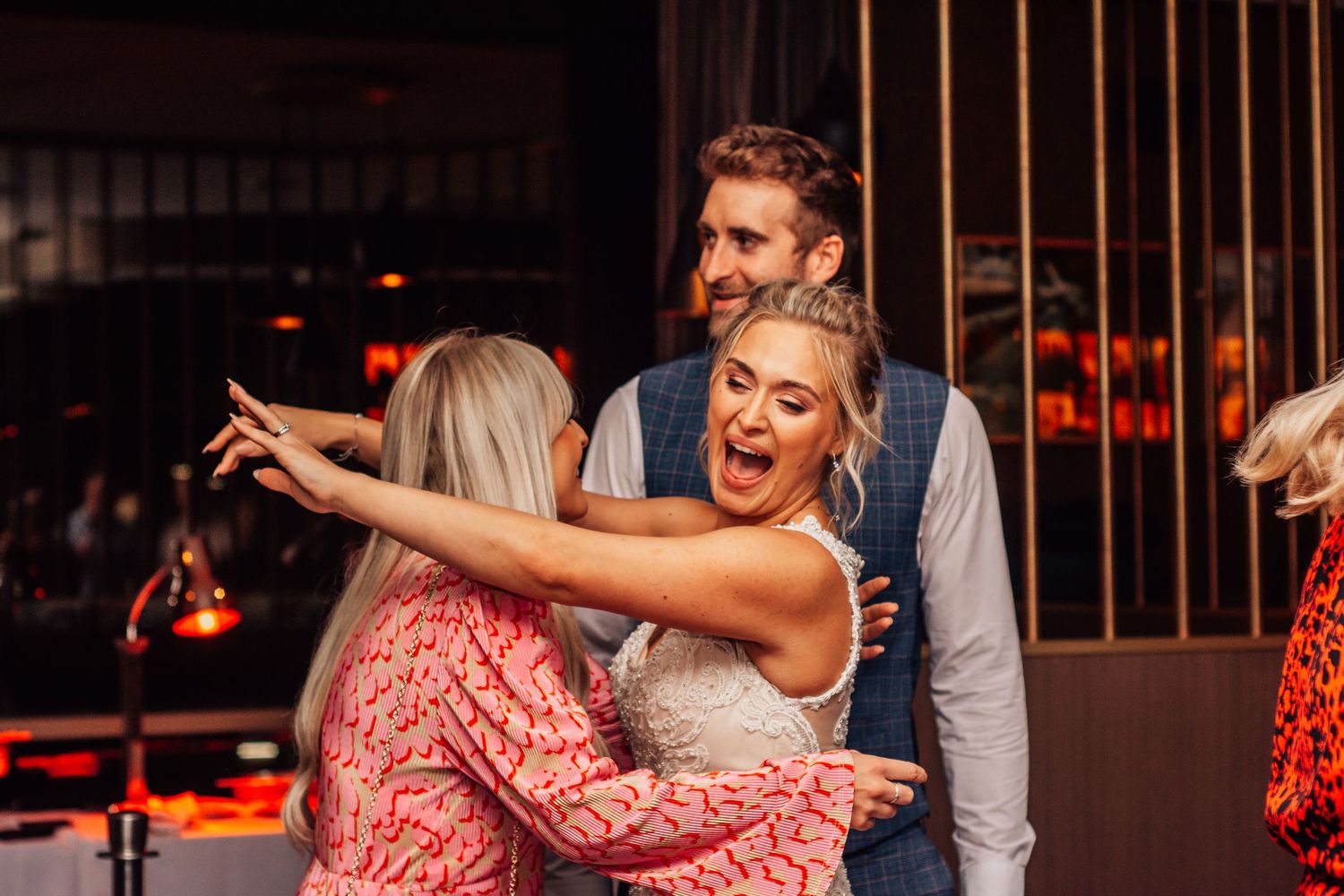 Joyful wedding guests hugging and laughing together at a stylish indoor reception venue.
