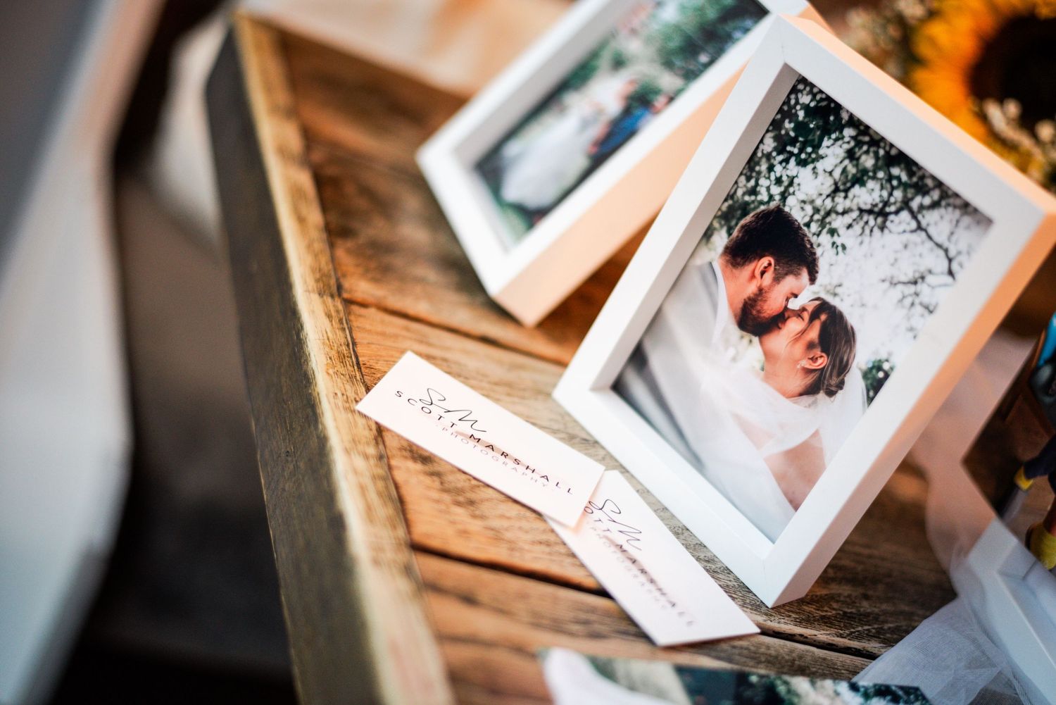 Framed wedding photos of a bride and groom displayed on a rustic wooden surface with elegant cards.