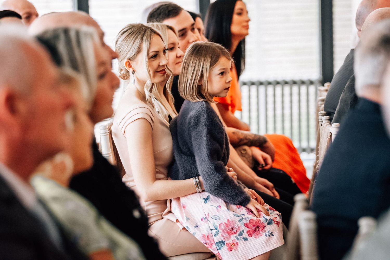 Wedding guests seated watching ceremony, including woman with young girl in floral dress.