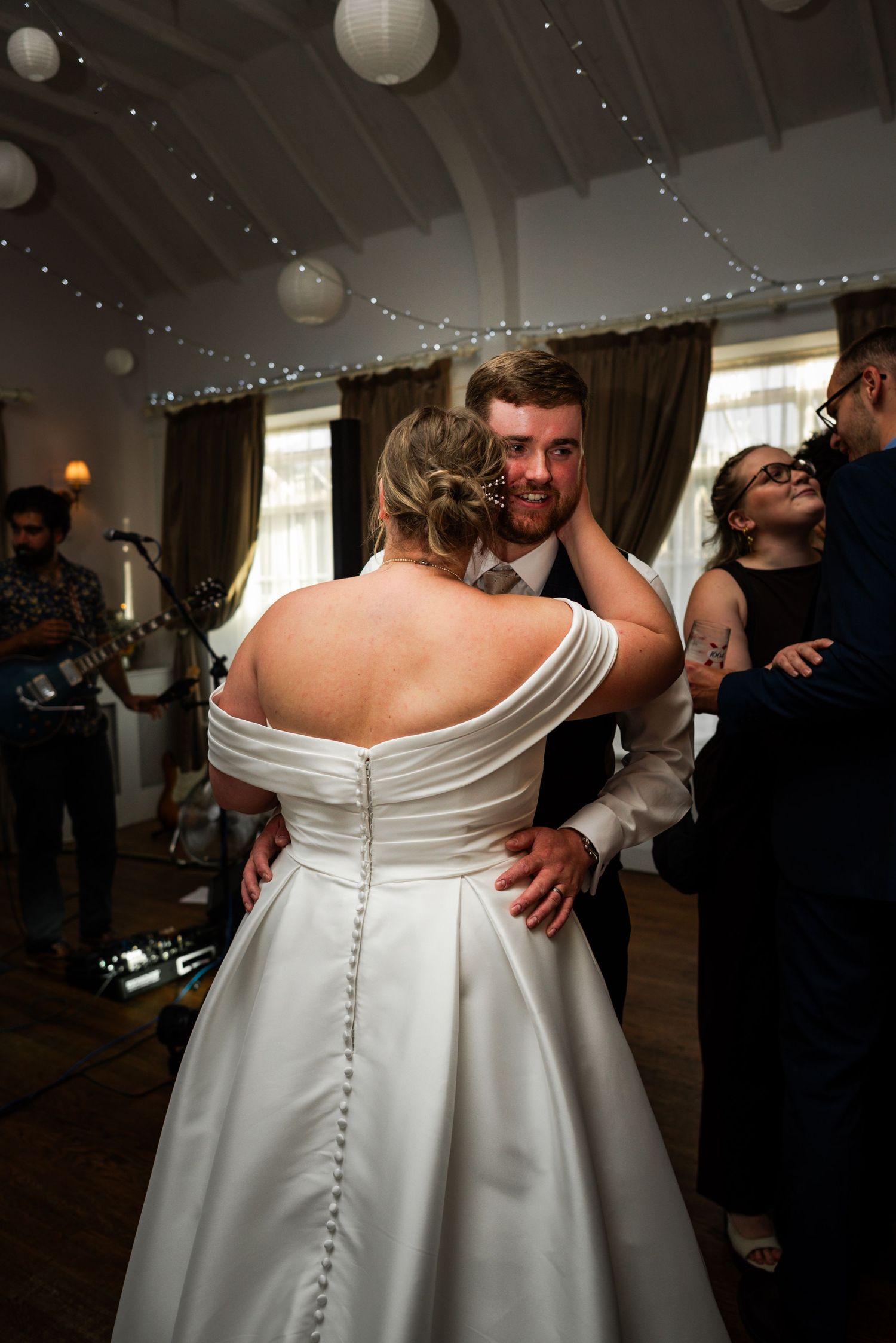 Groom smiling tenderly at bride during first dance at romantic wedding reception with fairy lights.
