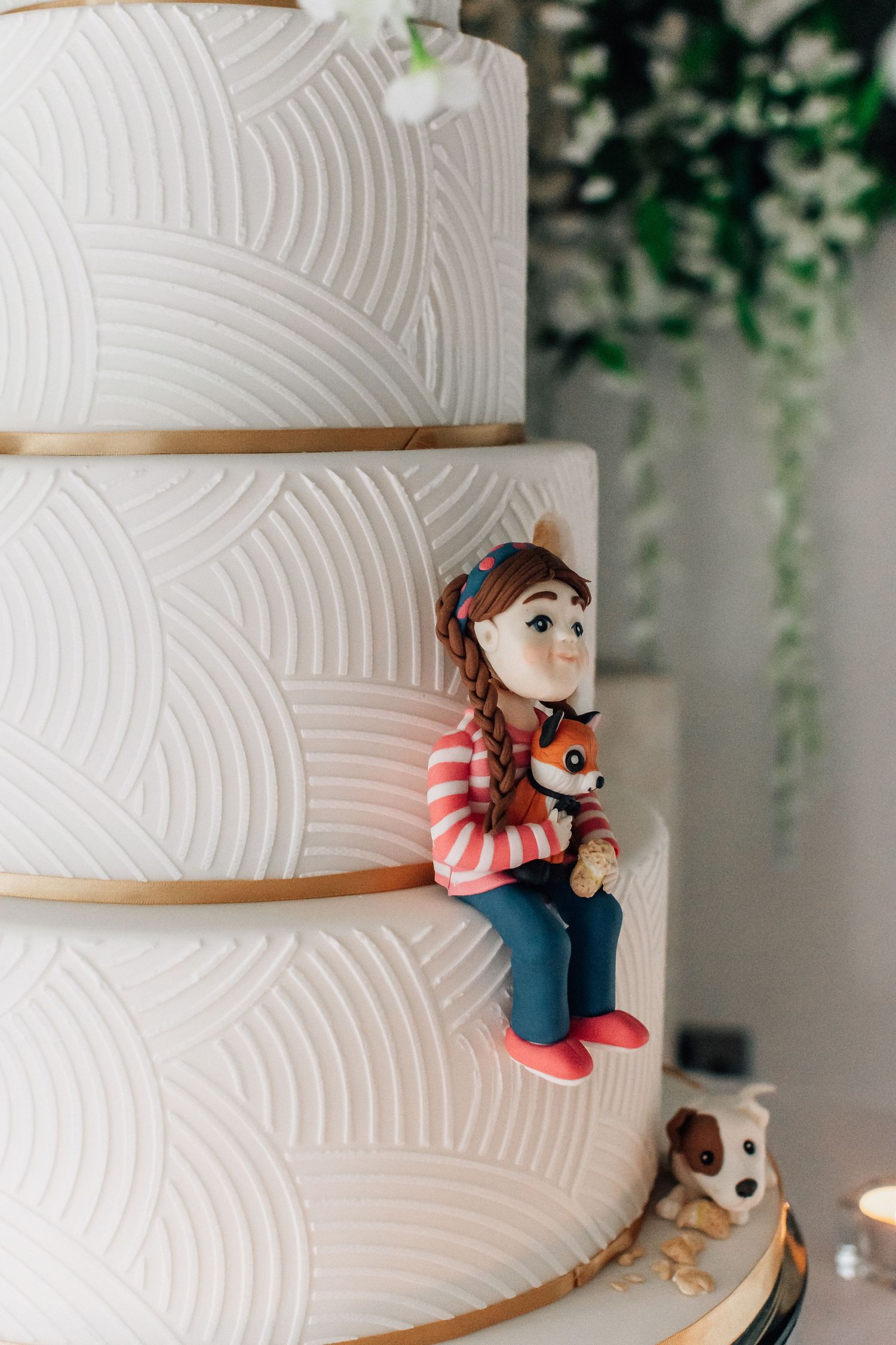 Elegant white tiered wedding cake with art deco pattern and whimsical fondant girl and fox figurine.