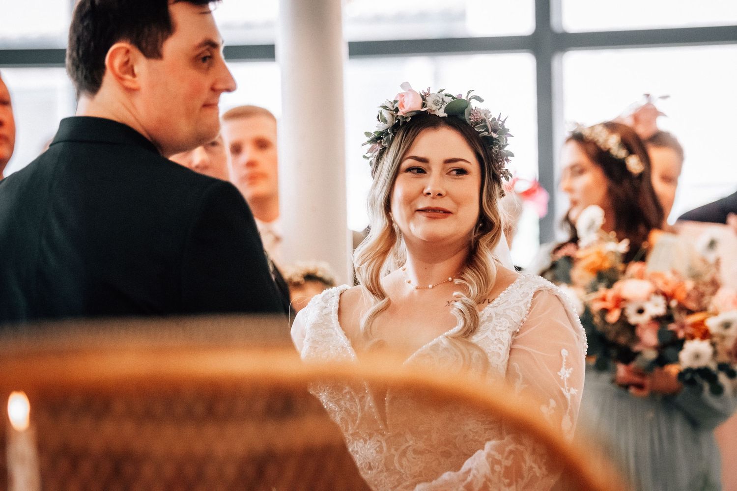Smiling bride wearing floral crown and lace wedding dress during ceremony.