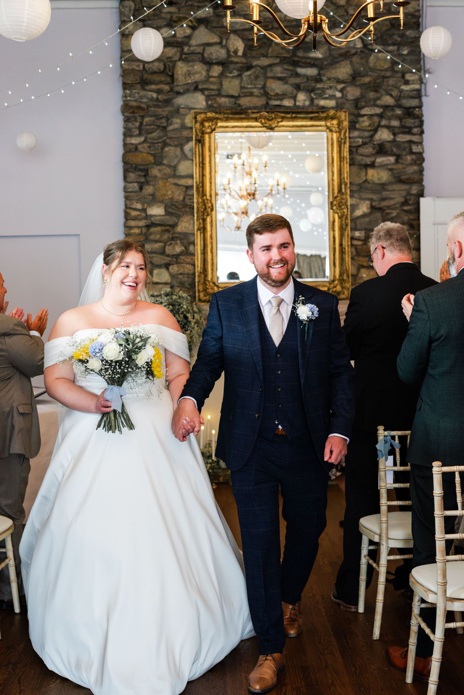 Bride and groom walk hand in hand down the aisle after wedding ceremony in rustic stone venue.