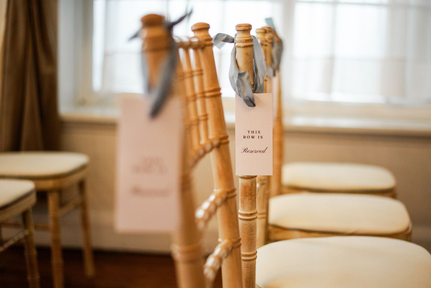 Gold chiavari chairs with reserved row signs and ribbon accents arranged for an elegant wedding ceremony.