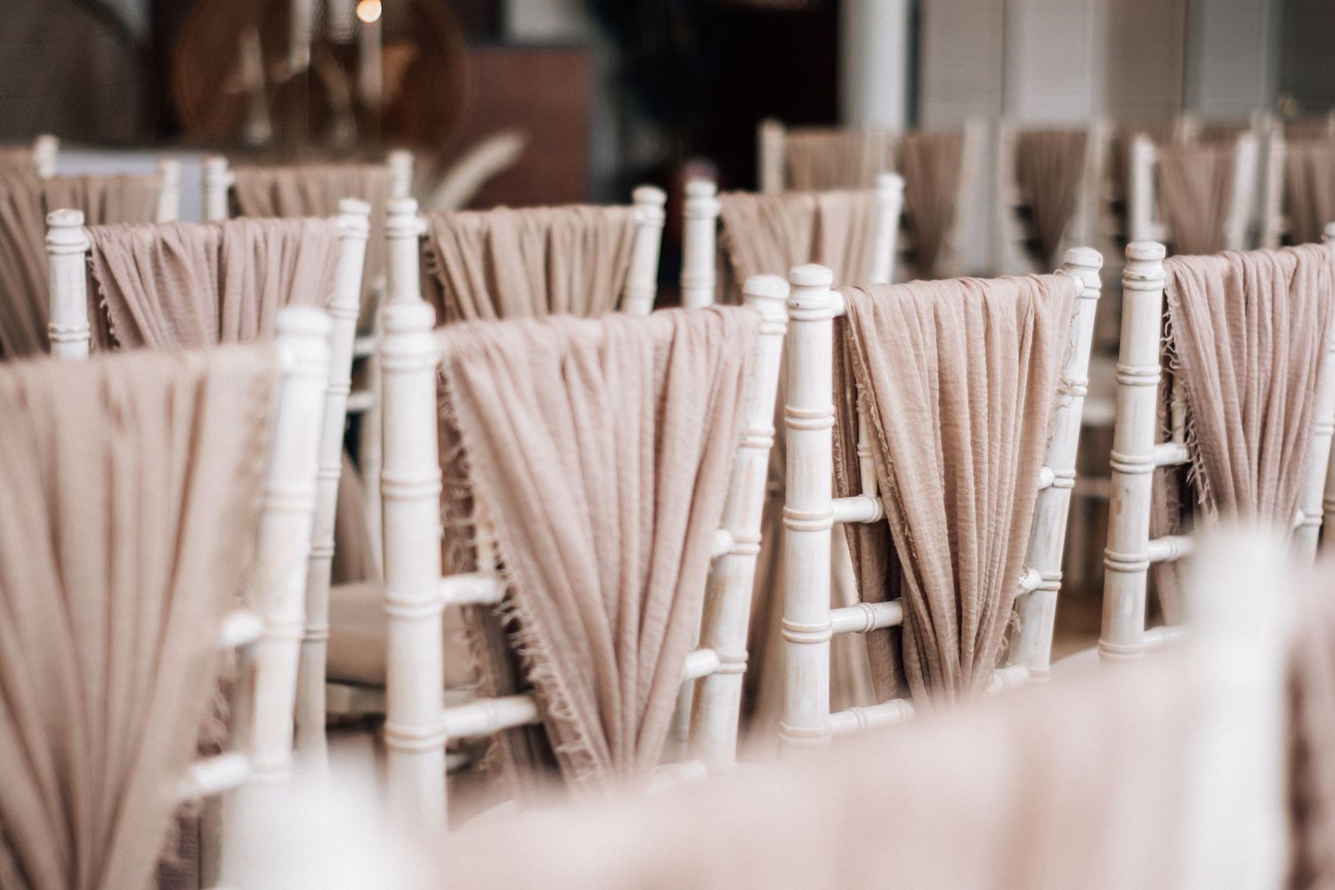 Elegant white Chiavari chairs adorned with flowing blush pink fabric sashes arranged in rows for a wedding reception.