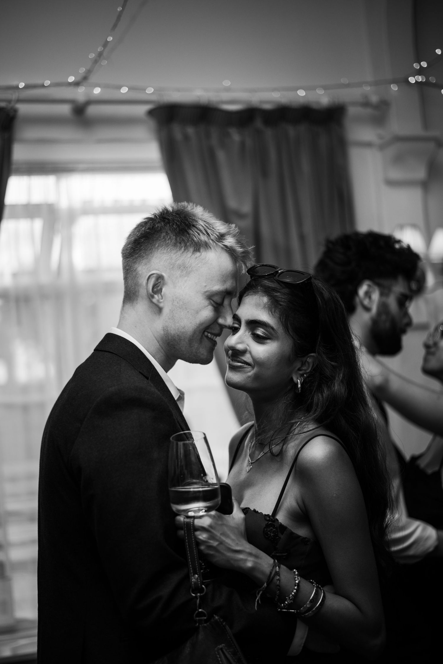 Couple shares romantic moment holding wine glass at elegant black and white wedding party.