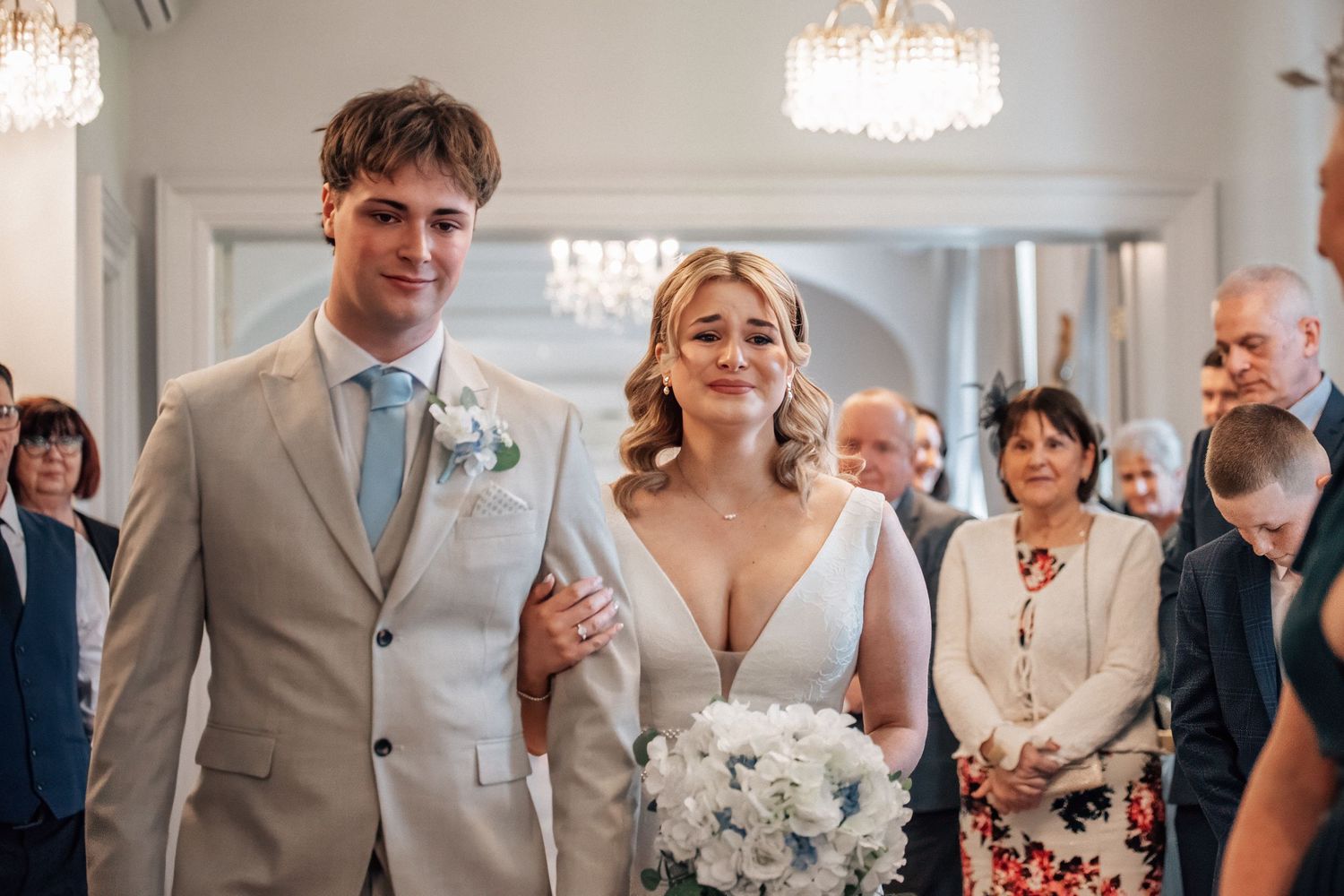 Smiling bride and groom walking down aisle in elegant venue during wedding ceremony.
