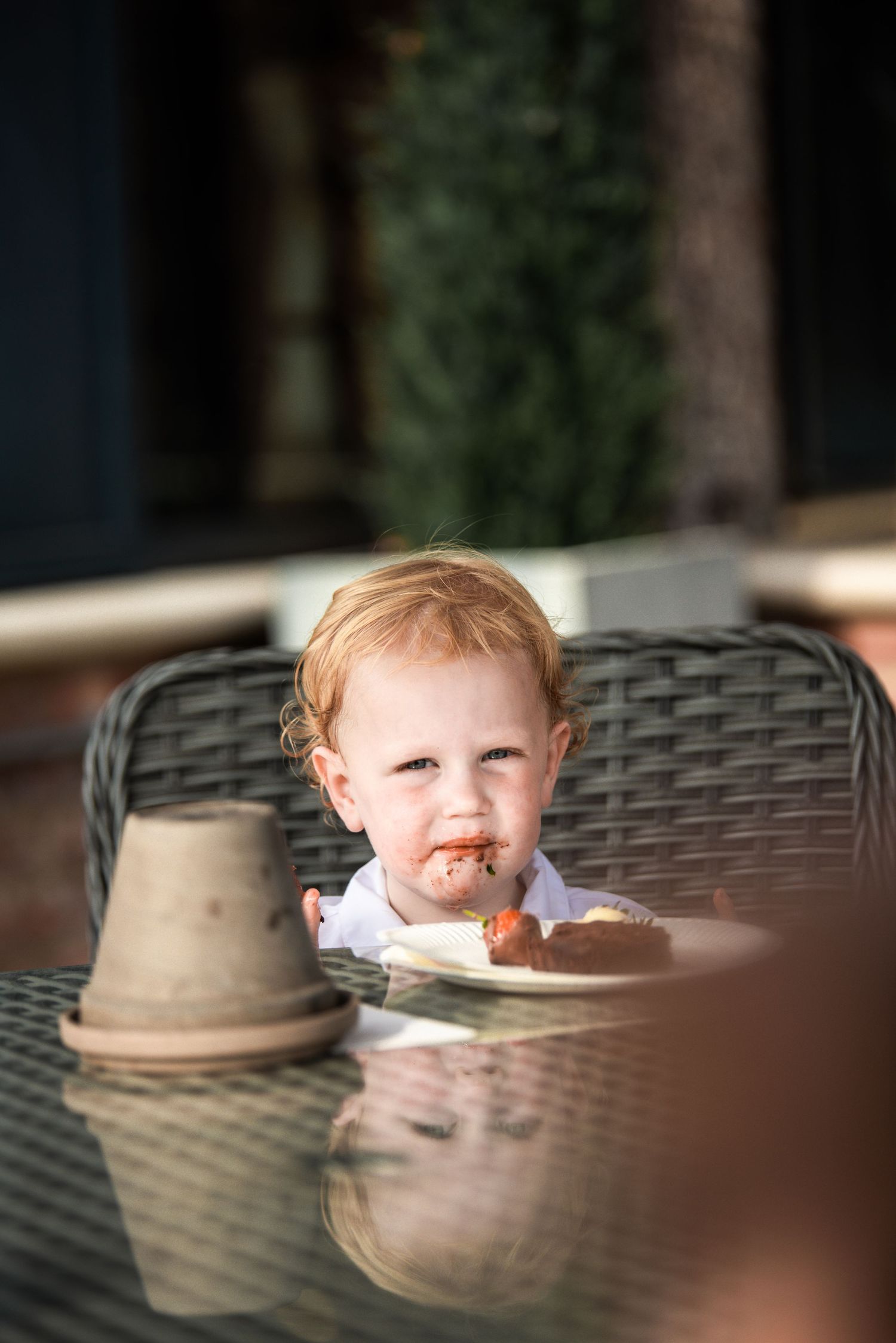 Cute toddler with messy face eating food at an outdoor patio table.