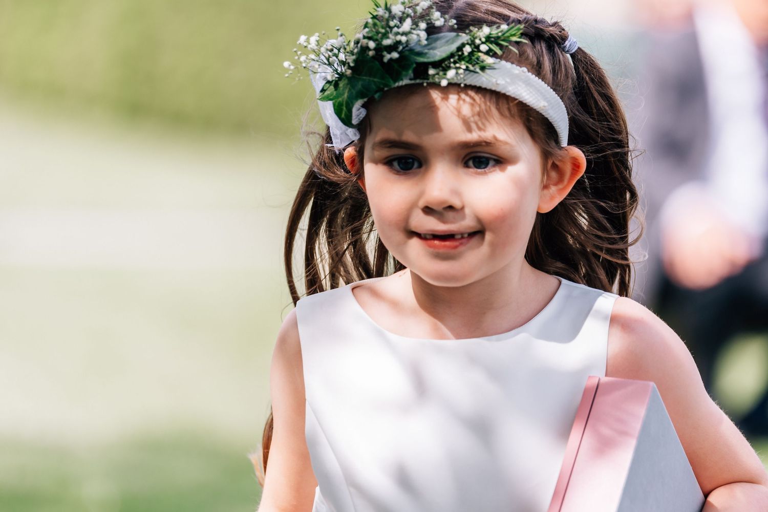 Young flower girl wearing floral crown runs outdoors during wedding ceremony.