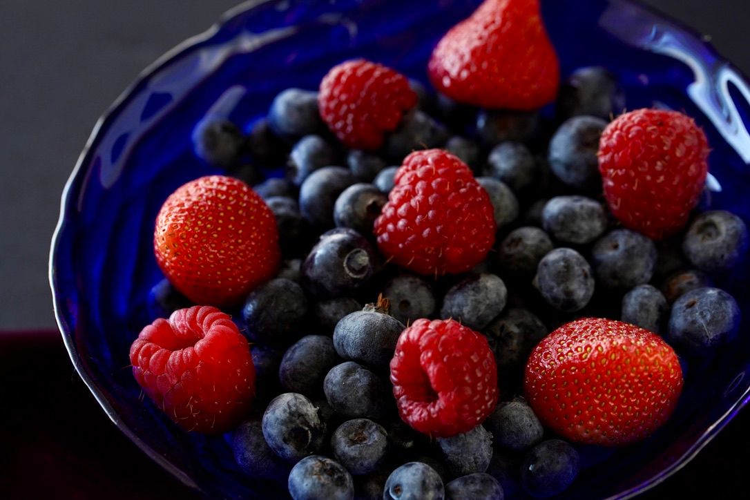 Fresh blueberries and raspberries arranged on blue ceramic plate.