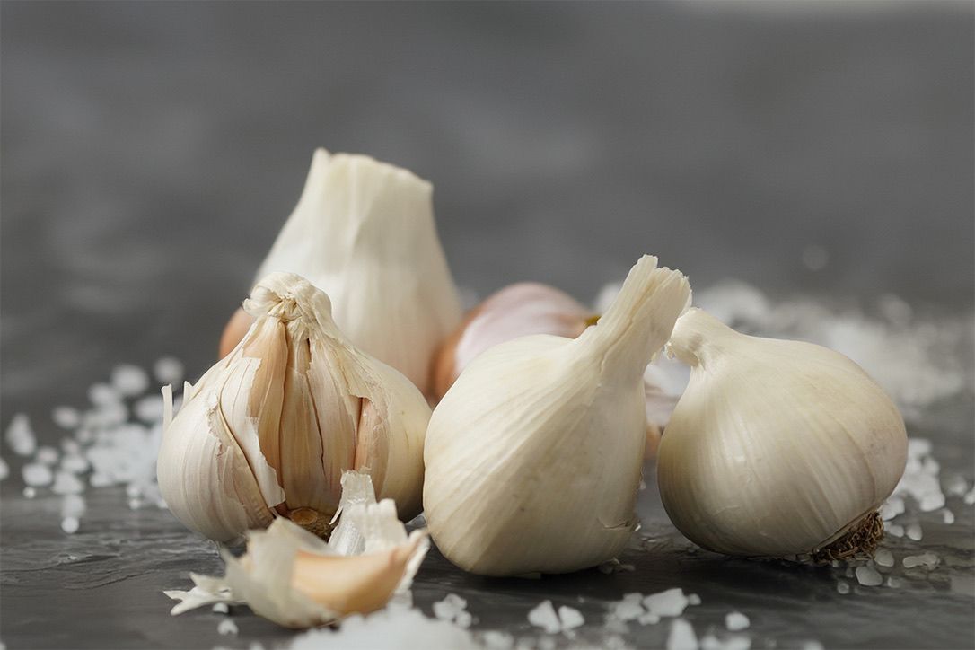 Fresh garlic cloves scattered with coarse salt on dark surface.