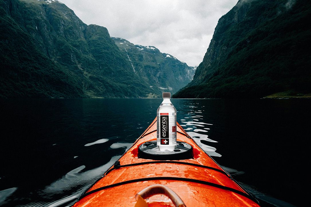 Orange kayak with Essentia water bottle on dark fjord waters surrounded by steep mountain cliffs.