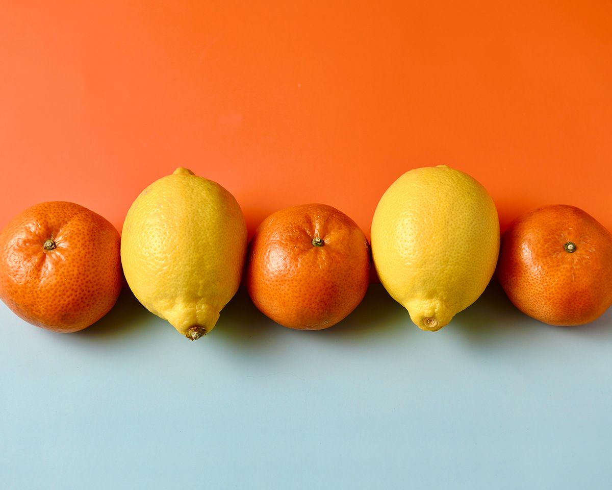 Fresh citrus fruits including oranges and lemons lined up against bright orange background.