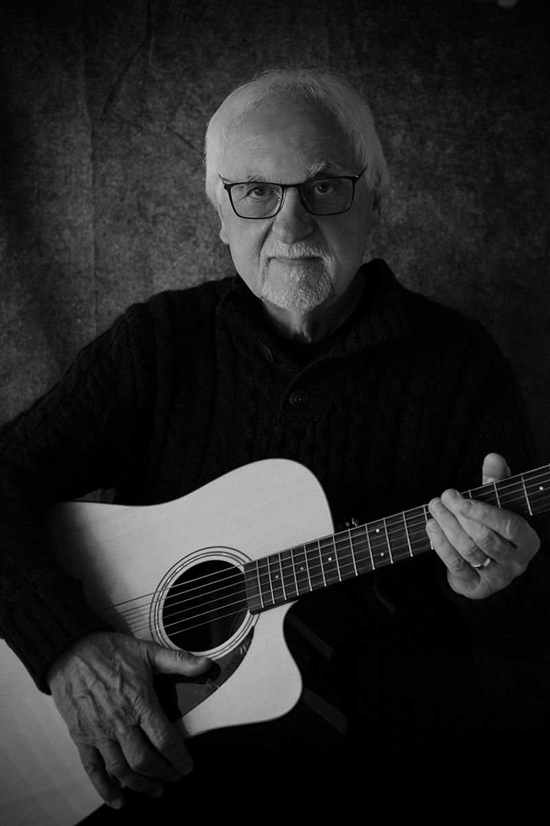Black and white series of a musician playing acoustic guitar in moody lighting.