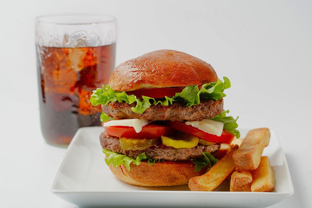 Juicy hamburgers with lettuce and fries served on white plates against a light background.