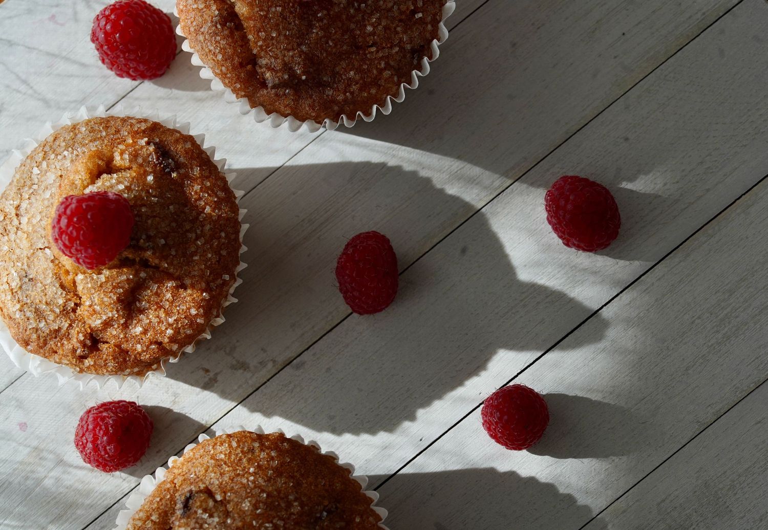 Golden brown muffins topped with sugar and fresh raspberries arranged on a wooden table.