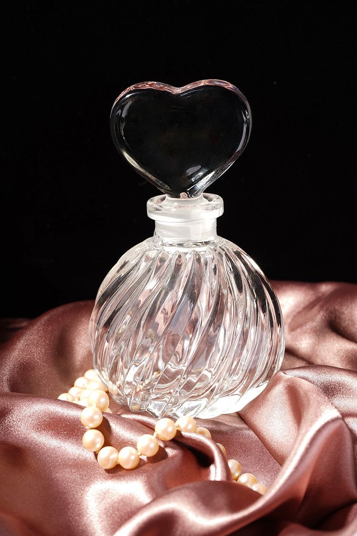 Crystal glass perfume bottle with elegant spiral design displayed on pink satin fabric with pearl necklace.