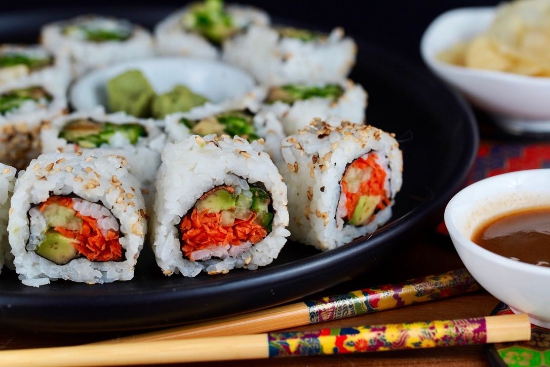 California sushi rolls with avocado and carrots served with chopsticks and dipping sauce.