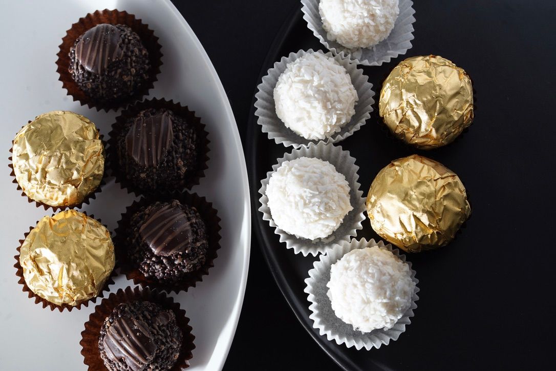 Elegant chocolate truffles wrapped in gold and silver foil arranged on black and white plate.