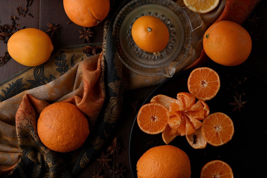 Whole and sliced oranges artistically arranged with spices on dark textured fabric.