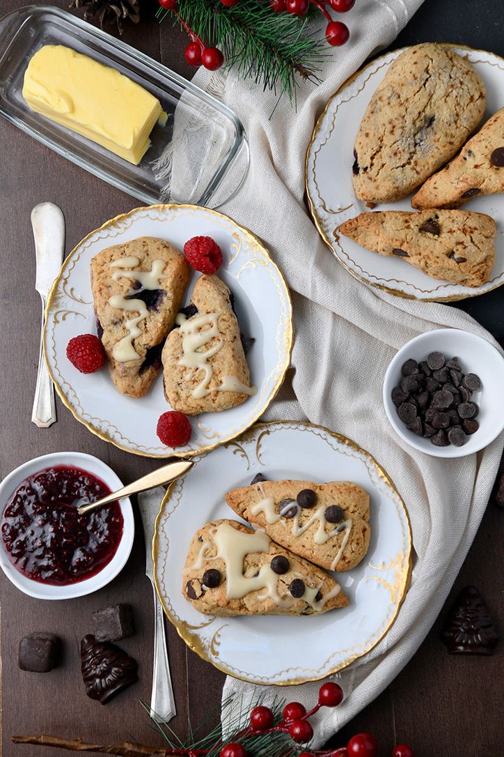 Chocolate chip scones served with butter and jam on white plates decorated with holiday greenery.