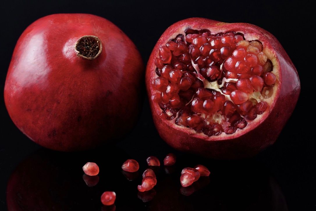 A whole and halved pomegranate with scattered arils on black background showing the fruit's vibrant red interior.