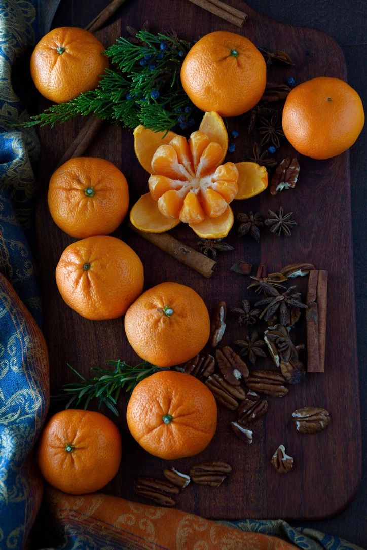 Fresh mandarin oranges and scattered spices on dark wooden surface with evergreen sprigs create festive holiday scene.