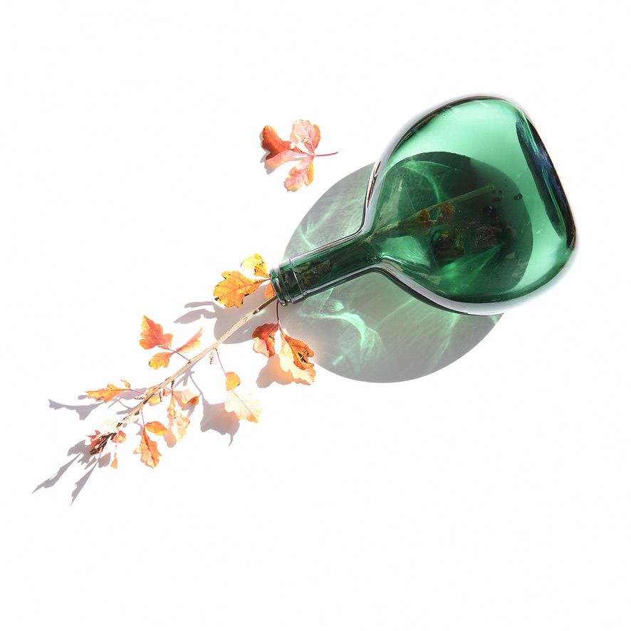 Tipped green glass bottle with orange autumn leaves on white background.