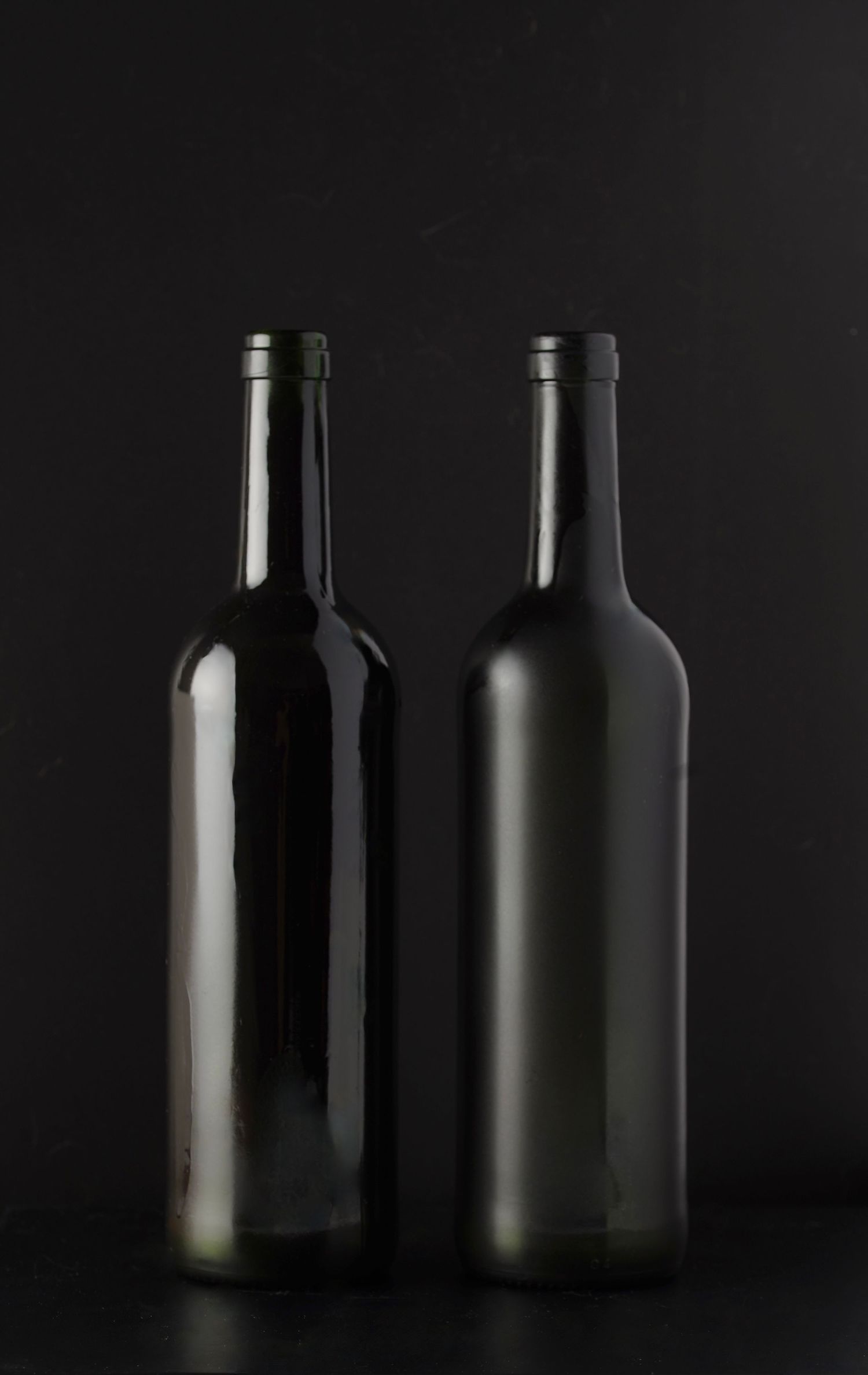 Two dark glass wine bottles casting shadows against a black background in dramatic lighting.