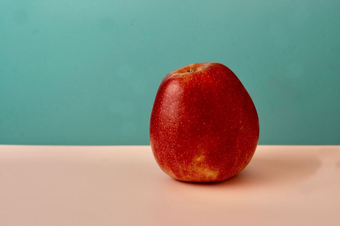 Fresh red apple on pink surface against turquoise background in minimalist composition.