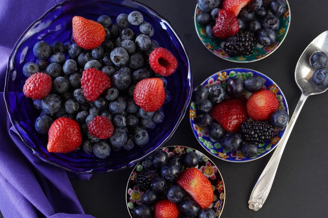 Fresh mixed berries including blueberries, strawberries and raspberries in blue bowls.
