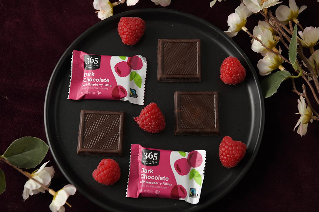 Dark chocolate squares and fresh strawberries arranged on a black plate with white flowers.