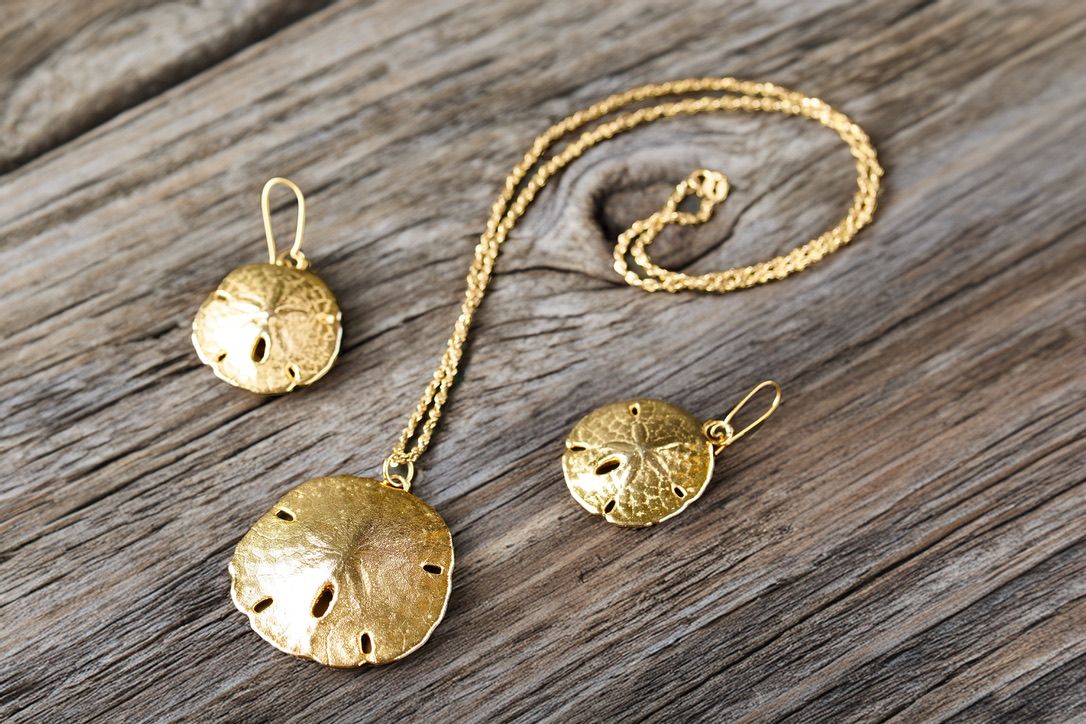 Gold sand dollar pendants and necklaces arranged on weathered wooden planks.