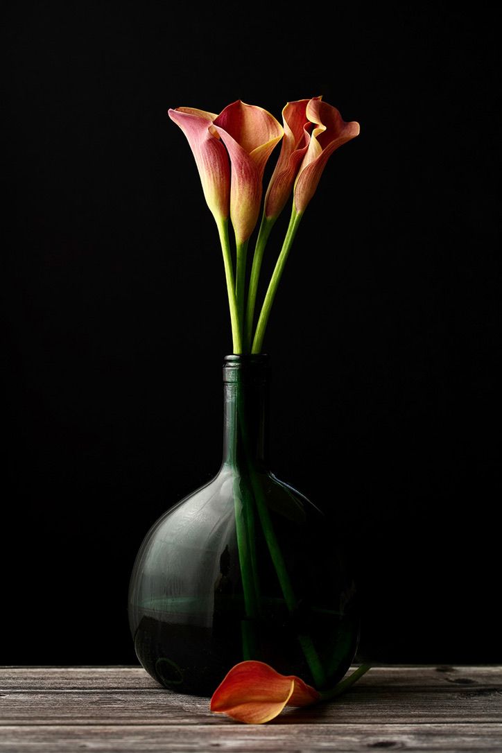 Elegant calla lilies arranged in a glass vase against dark background.