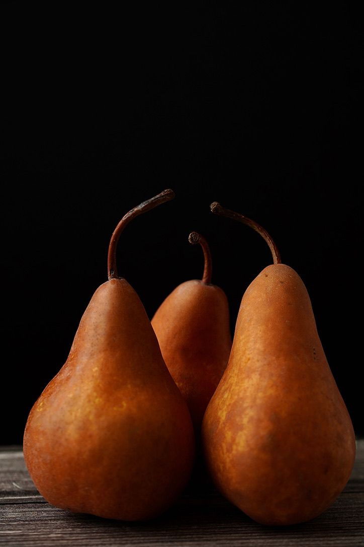 Three rustic brown pears against dark background on wooden surface.