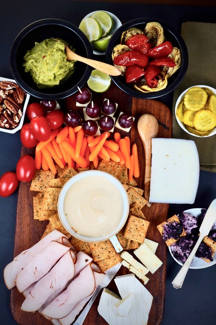 Colorful charcuterie board with meats, cheeses, vegetables, crackers and dips.