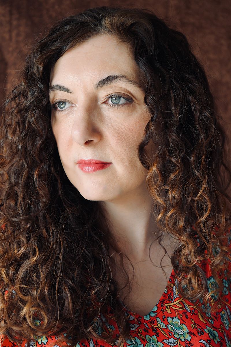 Dramatic portrait series with curly hair wearing a colorful patterned top against a brown backdrop.