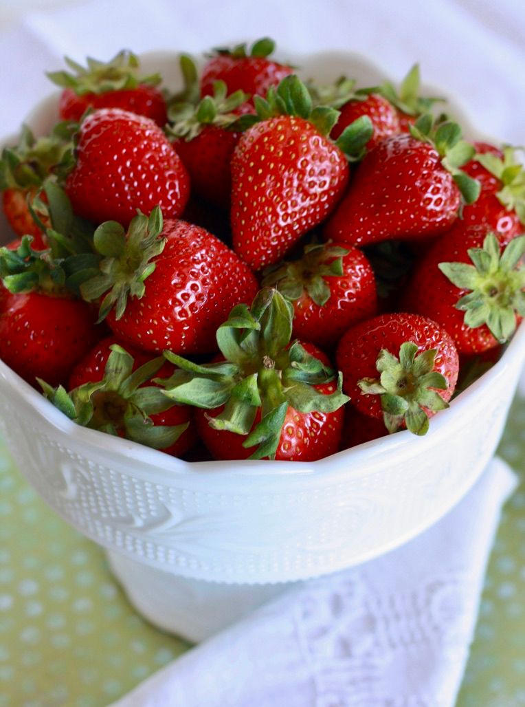 Fresh strawberries in white ceramic bowl on polka dot tablecloth.