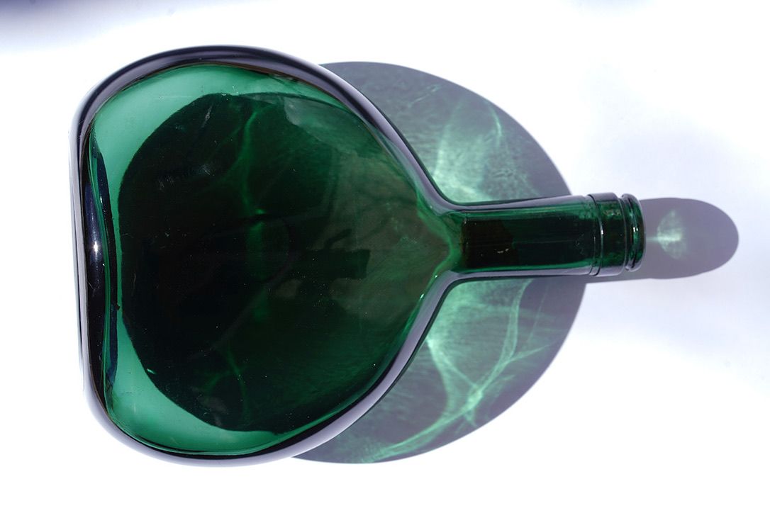 Overhead view of empty green glass wine bottle with dramatic shadow on white background.