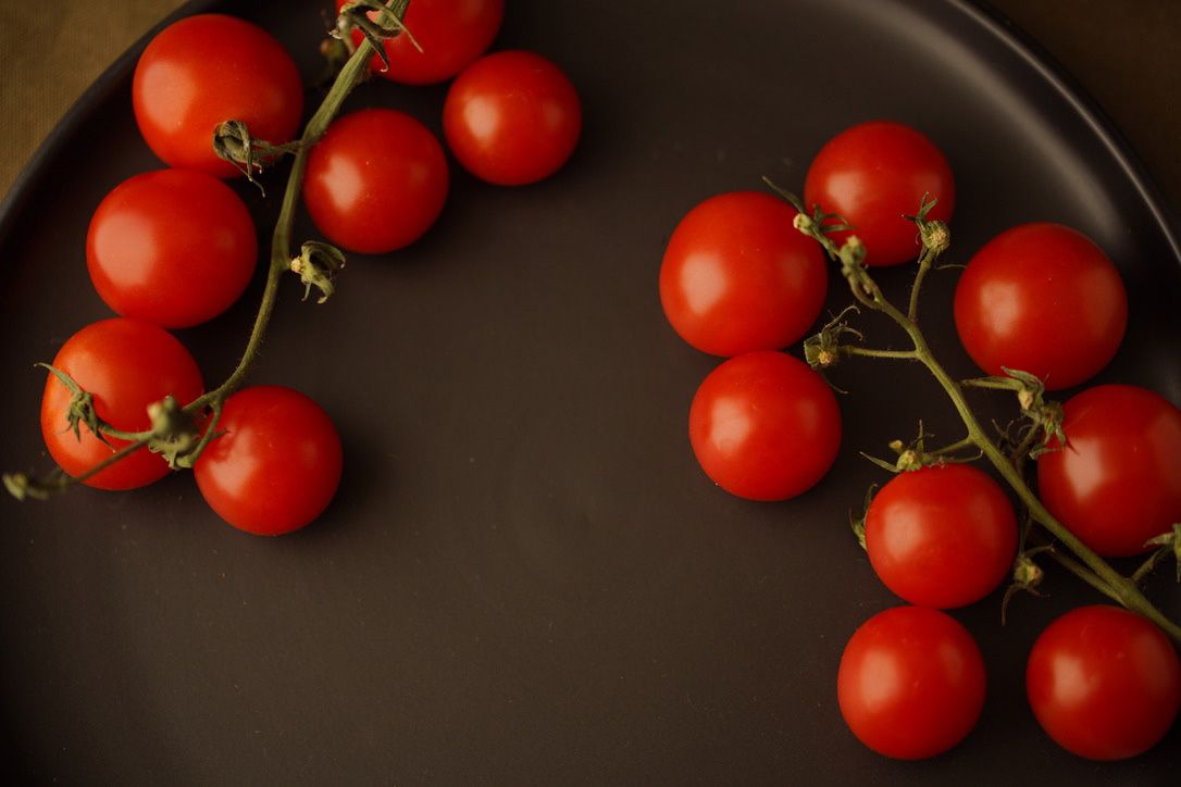 Ripe red cherry tomatoes on the vine against a dark background.