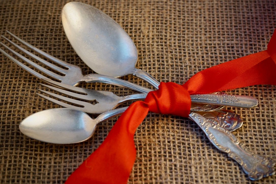 Antique silverware tied with red ribbon displayed on burlap texture.