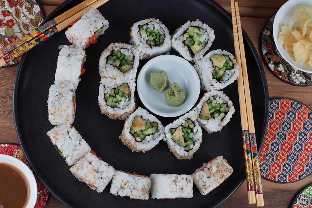 Assorted sushi rolls arranged on black plates with chopsticks and dipping sauces.
