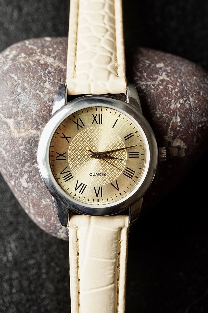 Elegant wristwatch with cream leather strap and roman numeral dial displayed on stone.